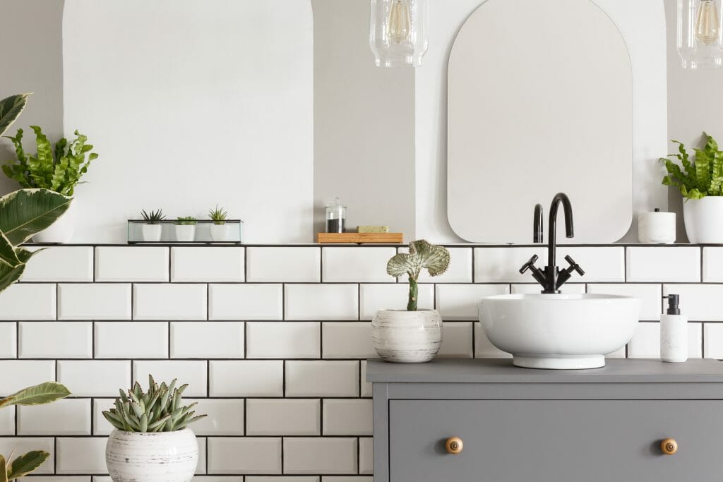Real photo of a sink on a cupbaord in a bathroom interior with tiles, mirror and plants