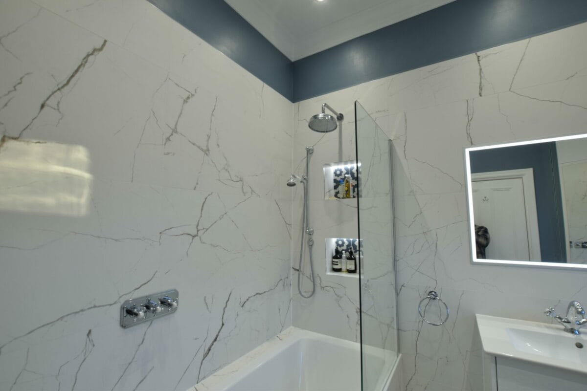 Luxury bath and shower room with large-format Calacatta marble-effect tiles, chrome traditional-style rainhead shower over bath, frameless glass screen, lit recessed niches and LED illuminated mirror — The London Bath Co., London