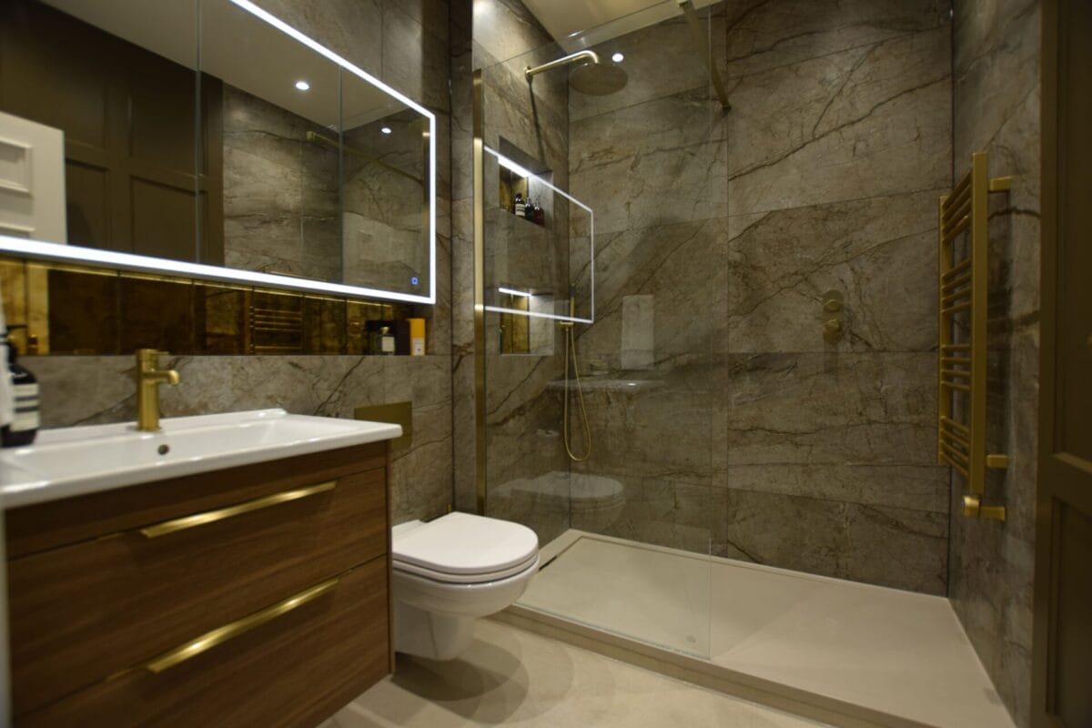 Luxury en suite bathroom with full-height marble-effect tiles, brushed gold fixtures, floating walnut vanity unit and frameless walk-in shower — bathroom renovation by The London Bath Co., London