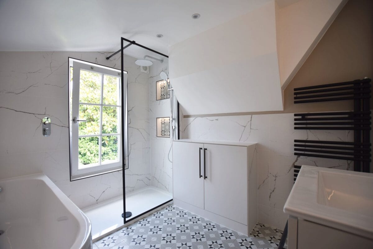 Spacious family bathroom in a London period property featuring black-framed walk-in shower, Calacatta marble-effect tiles, patterned floor tiles, rainhead shower and black ladder radiator — designed and installed by The London Bath Co.